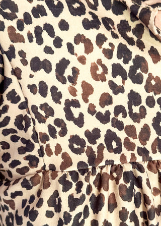 Close-up of a leopard print fabric with dark brown, black, and tan spots on a cream background, showing a ruffled seam and part of a collar.