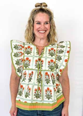 Flutter sleeve top with off white background and light green grid pattern-large orange florals with green stems/leaves in each grid. Olive green ribbon trim on sleeve and collar.  Olive green ribbon tie neck.  Olive green and orange trim on bottom band. 