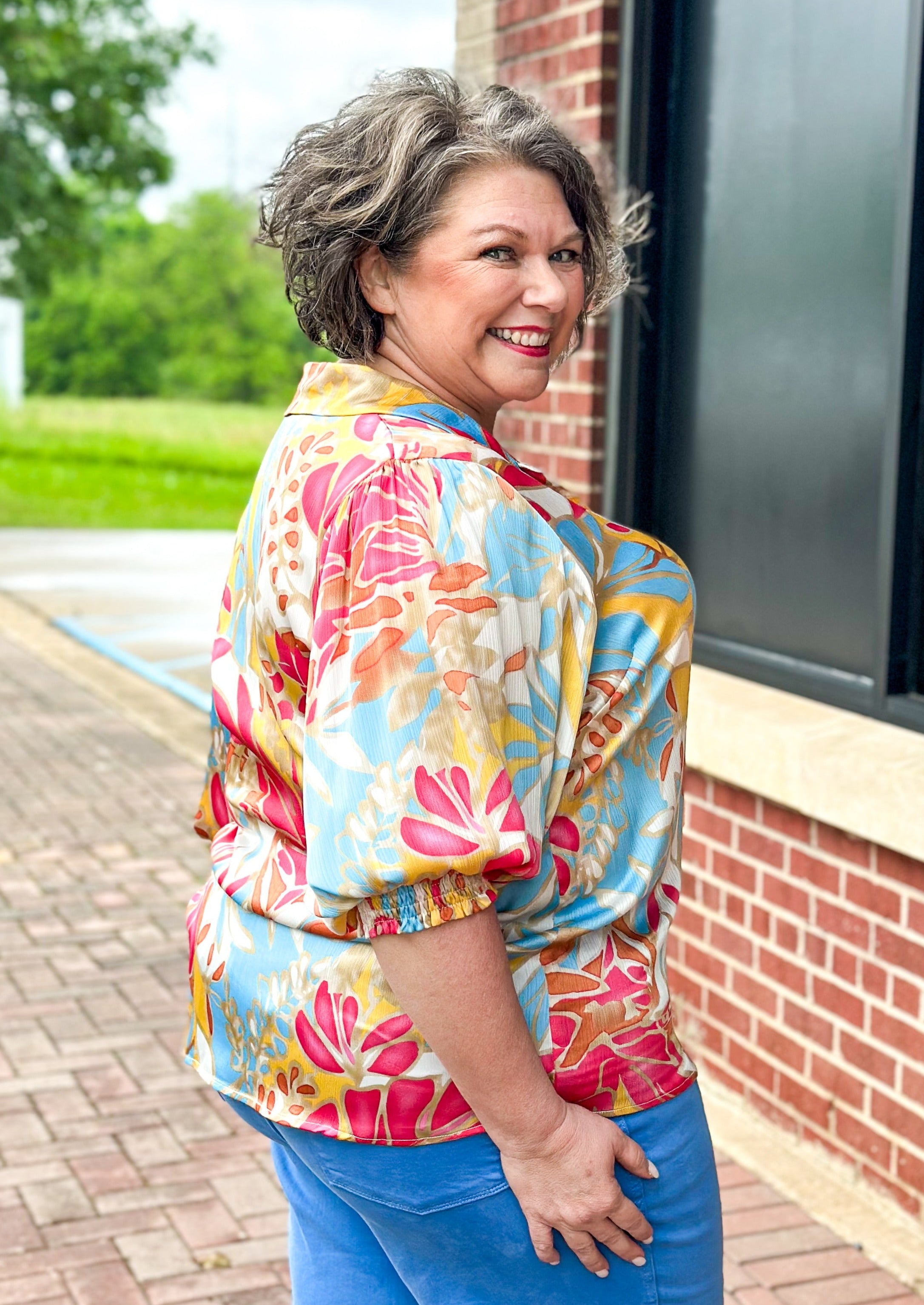 Leaf print 3/4 sleeve with v-neck, top button and collar - print is dark fuschia, gold, cream, orange and light blue - smocked cuff at edge of sleeve - crepe satin feel