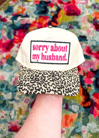 Cream snap back ball cap with a leopard bill and embroidered patch “sorry about my husband,” stitched in hot pink