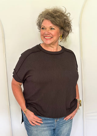 Woman wearing a brown top and blue jeans standing against a white background