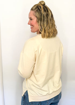 Lightweight cream long-sleeve top with colorful chenille patch letters spelling “HAPPY”