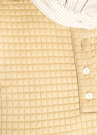 Close up of long-sleeve textured neutral tan dress with a striped ruffle neckline, partial button front, and matching striped sleeve cuffs