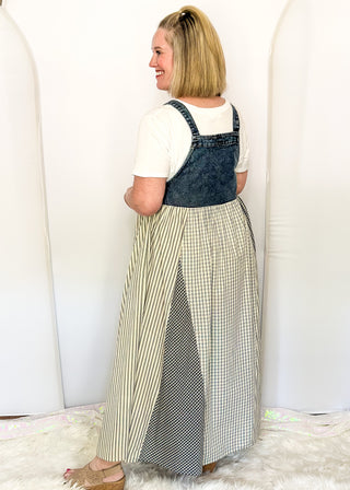 side view of woman modeling a denim overall style dress with gingham floral pattern.