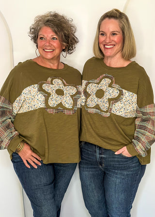 Two women wearing an olive green  patchwork top with floral fabric pattern on the front and plaid long sleeves. 