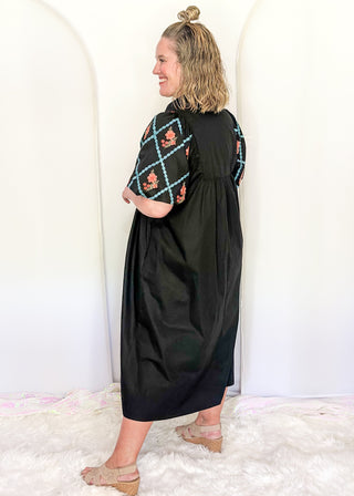 Women wearing a black midi dress with embroidered puff sleeves and a smocked bodice