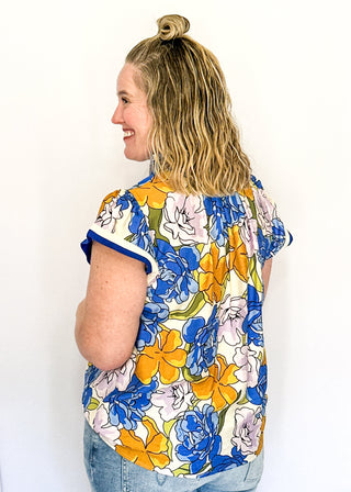 Floral top featuring blue, yellow, and lavender blooms with blue contrast trim on neckline and sleeves.