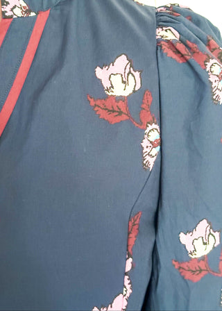 Close up of floral navy dress featuring v-neckline, burgundy piping, and puff sleeves