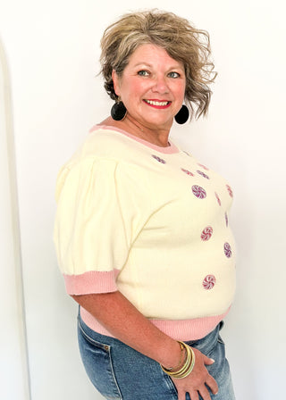 Cream short sleeve sweater with puff sleeves, pink trim, and sequin peppermint candy accents on the front