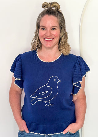 woman in blue ruffle sleeve sweater with white stitched bird