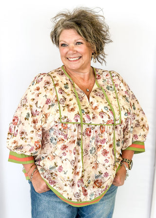 Soft floral Babydoll top with 3/4 puff sleeve, orange and green strip detail on banding of hem and sleeve. green ribbon detail on the front and tie at the collar. 