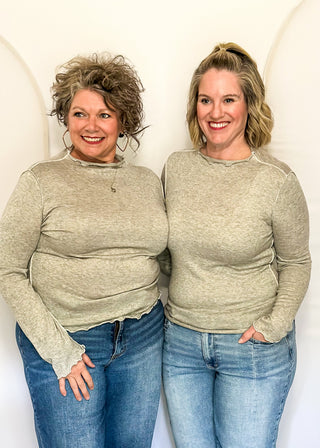 Two women standing side-by-side wearing matching heathered sage green long-sleeve mock neck knit tops and blue jeans, posing in front of a white arched studio backdrop.