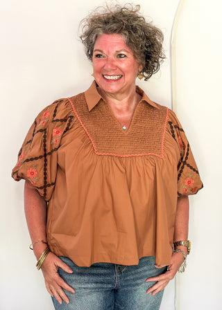 woman in chestnut poplin puff sleeve top with embroidery. 