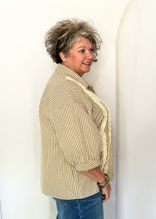 A woman with short curly gray hair models a beige and white striped button-down shirt with a cream lace-trimmed collar, paired with blue jeans, standing against a white studio backdrop.