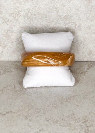 Light brown bangle bracelet displayed on a stand 