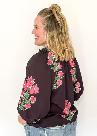 Woman wearing a black blouse with pink floral embroidery against a white background