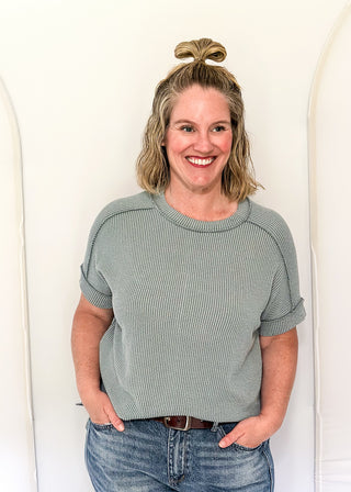 Woman wearing a gray ribbed sweater and blue jeans against a white background
