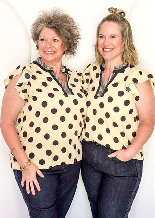 Women's cream blouse with black polka dots, striped split neckline, and flutter sleeves.
