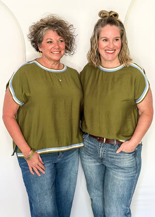 Two women wearing olive green tops with cap sleeves and crew necklines, styled with jeans.