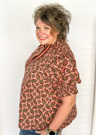 Bubble sleeve V-neck short sleeve top with terracotta, brown and green print. Ribbon detail down the front in brown and terracotta. 