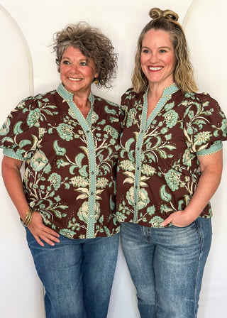two women standing in a brown, cool blue and cream button up top and jeans.