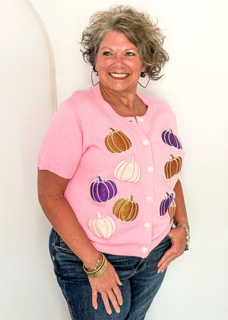 Woman wearing a pink sweater with purple, orange, and light pink glitter pumpkins. 