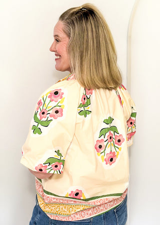 Women's short sleeve ecru top with pink floral bundles and decorative hem and collar. 