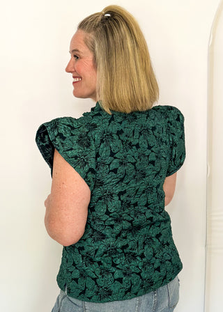 side view of woman wearing forest green jacquard flutter sleeve blouse with a floral pattern