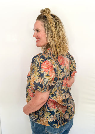 Short puff sleeve navy floral top. Florals are terracotta and coral.  V-neck with coral piping detail on chest.