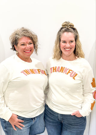 Light Ivory Long sleeve top with terracotta leaves and pink pumpkin patches sewn on the sleeves. "Thankful" chenille patches across the chest in pink and terracotta. 