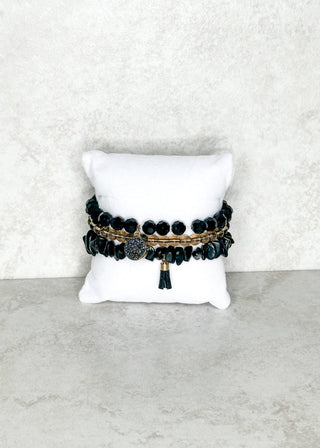 Set of black beaded bracelets on a white cushion against a light gray background
