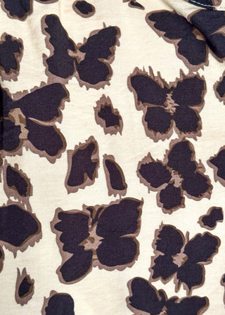 A close-up of a fabric pattern featuring stylized dark brown butterfly and flower motifs on a warm cream background.