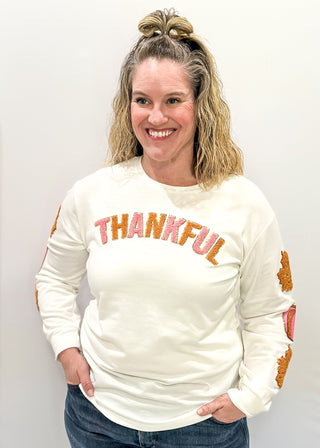 Light Ivory Long sleeve top with terracotta leaves and pink pumpkin patches sewn on the sleeves. "Thankful" chenille patches across the chest in pink and terracotta. 