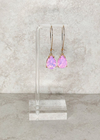 Teardrop gemstone dangle earrings in pink. Displayed on a stand 