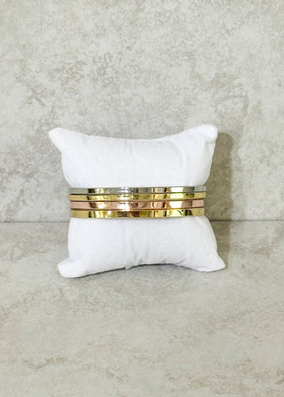 White pillow with set of 4 bangles on a textured gray background