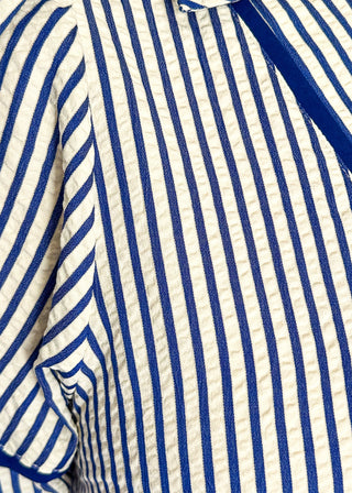 Close up of blue and cream striped midi dress with short sleeves, split V-neckline with contrast trim, pockets, and a relaxed fit.