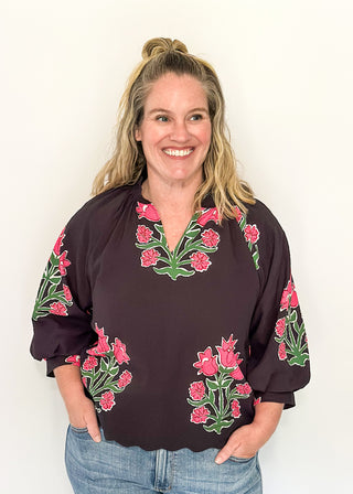 Woman wearing a black blouse with floral embroidery against a white background