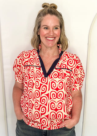 Red swirl print blouse with navy contrast trim, puff sleeves, and split neckline detail.