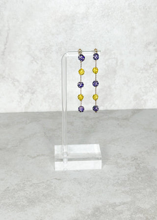 Set of colorful beaded earrings on a clear stand against a light gray background