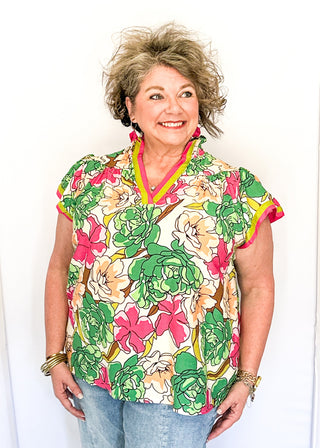 Bright floral blouse in pink, green, and yellow tones with split neckline and cap sleeves.
