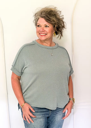 Woman wearing a green textured sweater and blue jeans against a white background