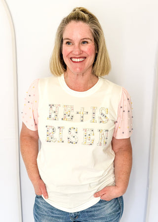 Off white short sleeve shirt with colorful embellished text and pink statement sleeves with decorative pearl studs.