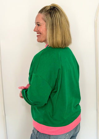 side view of woman wearing a green long sleeve mock neck top with pink contrast sleeve  and "OH WHAT FUN" embroidered letter patches.