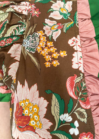 pink and golden botanicals on a brown background.  Short ruffle sleeves, v-neck ruffle collar in pink and green 