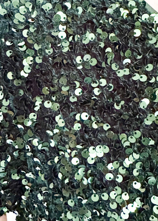 A close-up of a black sequined fabric with dense, shiny circular sequins reflecting light.