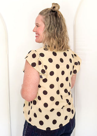Women's cream blouse with black polka dots, striped split neckline, and flutter sleeves.