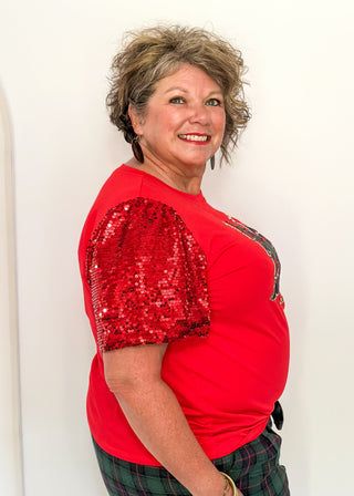 Person wearing a red sequin-sleeve top and plaid pants against a white background