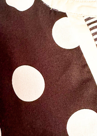 close up of black tiered polka dot dress with flutter sleeves and striped contrast trim around the neckline and tiers