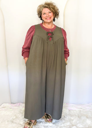 Charcoal gray sleeveless woven jumpsuit with ribbon tie neckline, pockets, and flowy wide-leg fit.