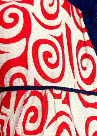 Close up of red swirl print blouse with navy contrast trim, puff sleeves, and split neckline detail.